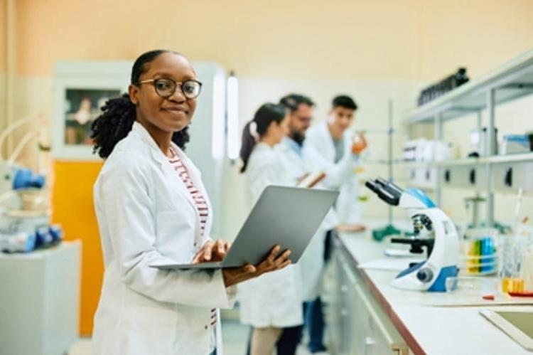 Happy African American scientist using laptop while working in lab and looking at camera.